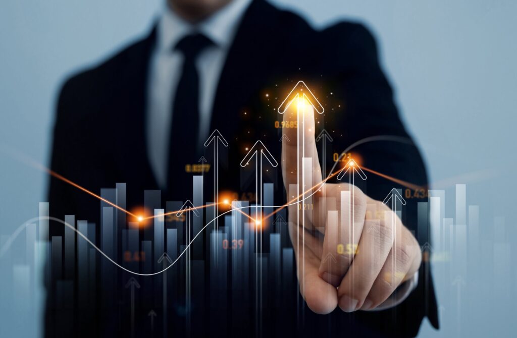 A person in a suit points at an arrow on a graph going upward.